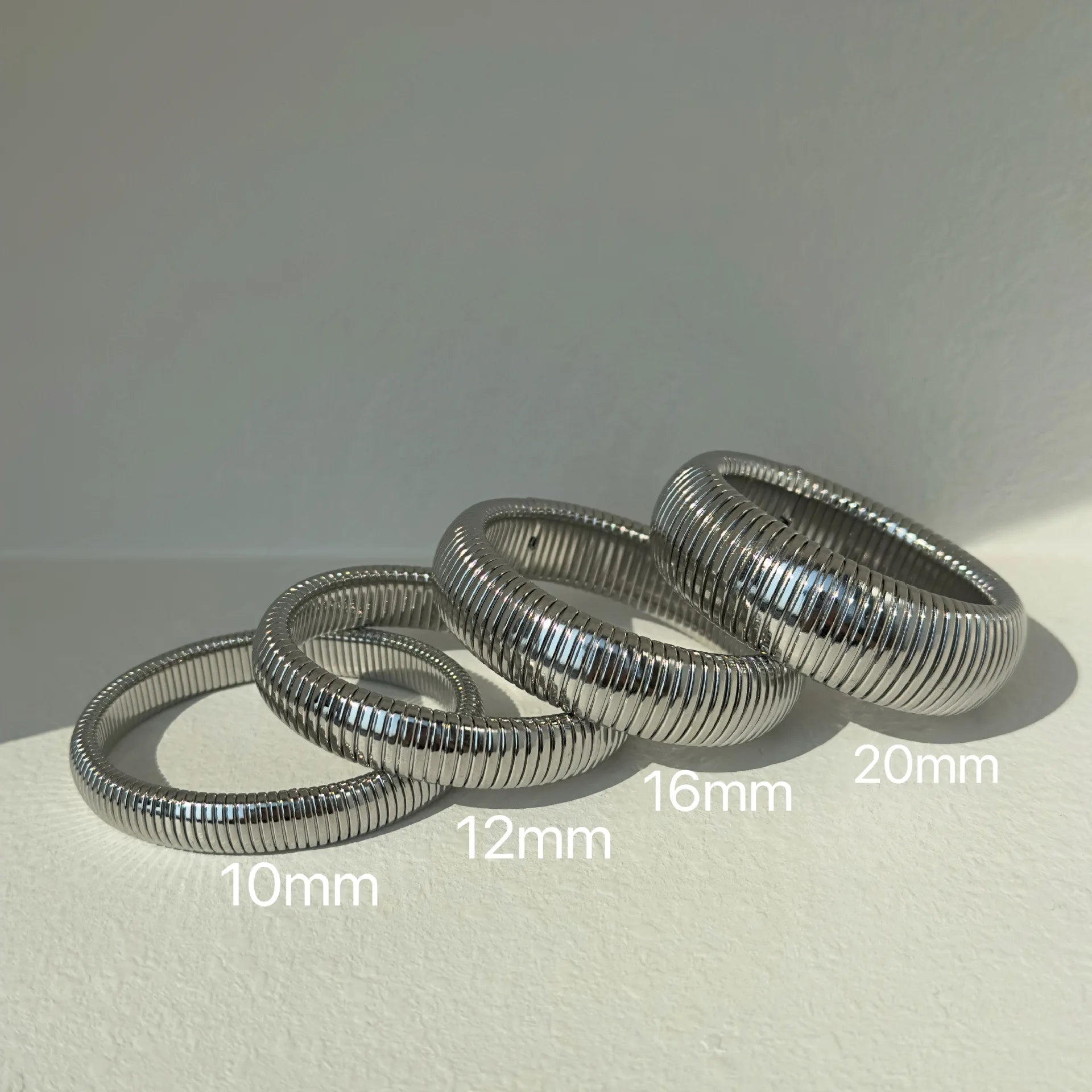 The image depicts a stylish bracelet with a ribbed design in a shiny rose gold color, suggesting it is made of 18k gold plated titanium. The bracelet features a twisted, interwoven appearance, giving it a unique and fashionable look. It appears to be a single, continuous band without clasps, showcasing its design.