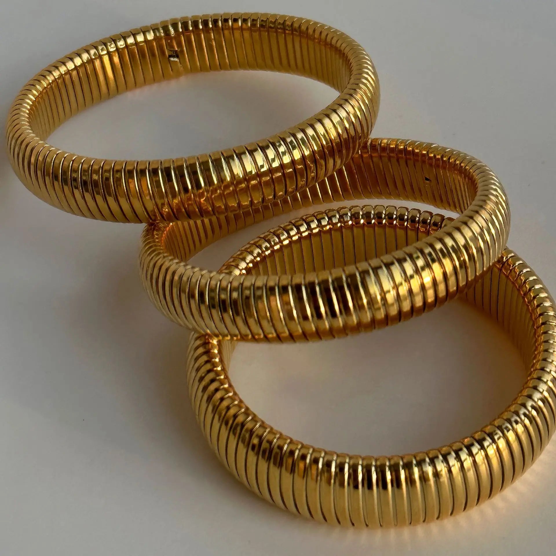 The image depicts a stylish bracelet with a ribbed design in a shiny rose gold color, suggesting it is made of 18k gold plated titanium. The bracelet features a twisted, interwoven appearance, giving it a unique and fashionable look. It appears to be a single, continuous band without clasps, showcasing its design.