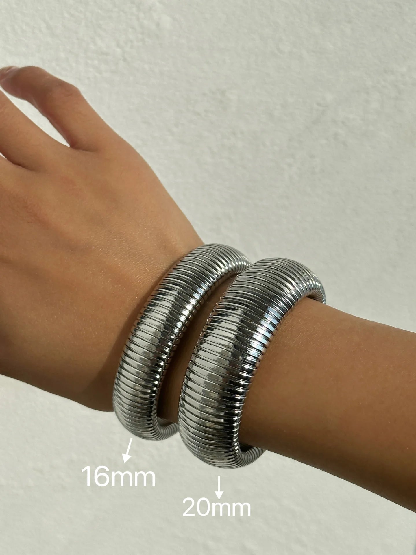 The image depicts a stylish bracelet with a ribbed design in a shiny rose gold color, suggesting it is made of 18k gold plated titanium. The bracelet features a twisted, interwoven appearance, giving it a unique and fashionable look. It appears to be a single, continuous band without clasps, showcasing its design.