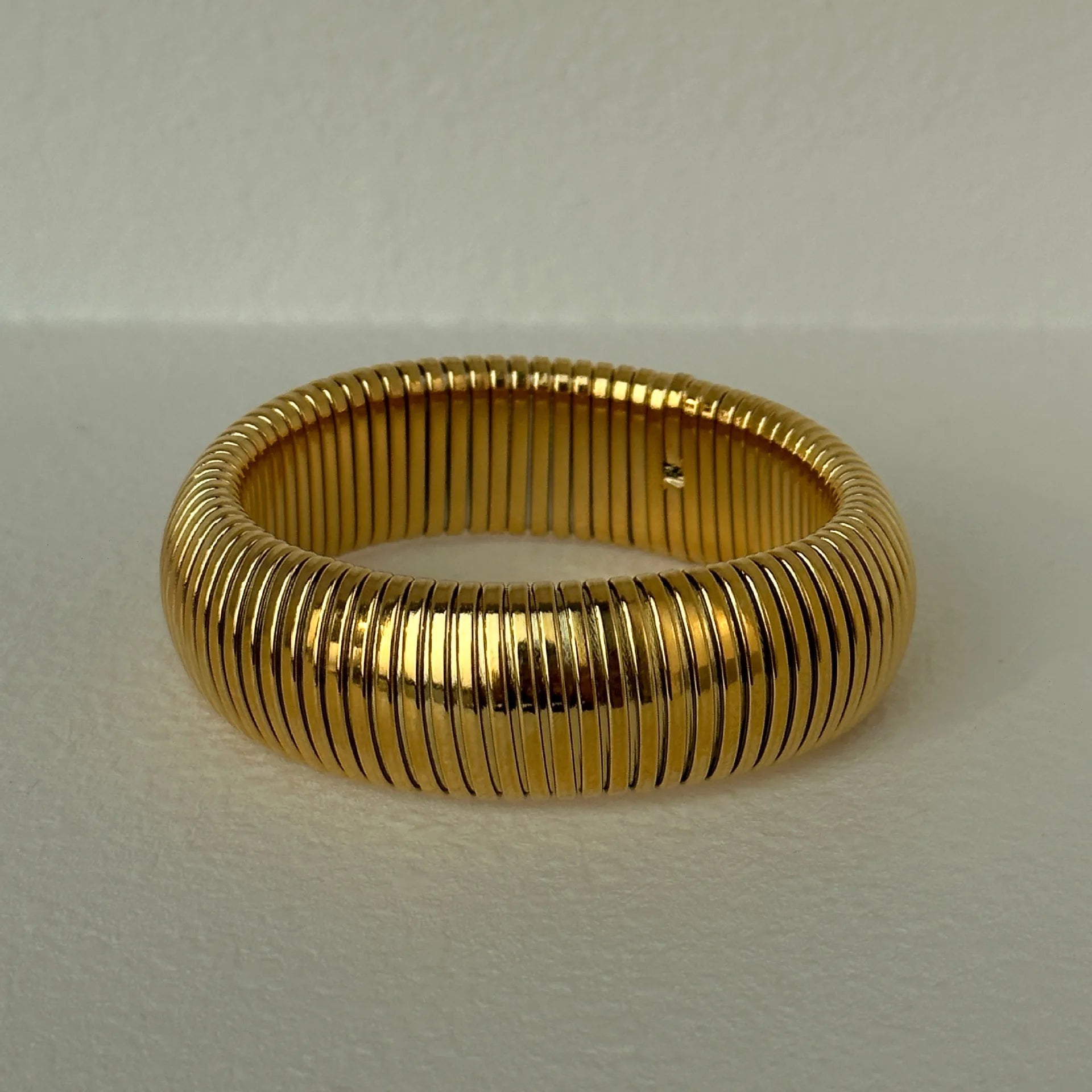 The image depicts a stylish bracelet with a ribbed design in a shiny rose gold color, suggesting it is made of 18k gold plated titanium. The bracelet features a twisted, interwoven appearance, giving it a unique and fashionable look. It appears to be a single, continuous band without clasps, showcasing its design.