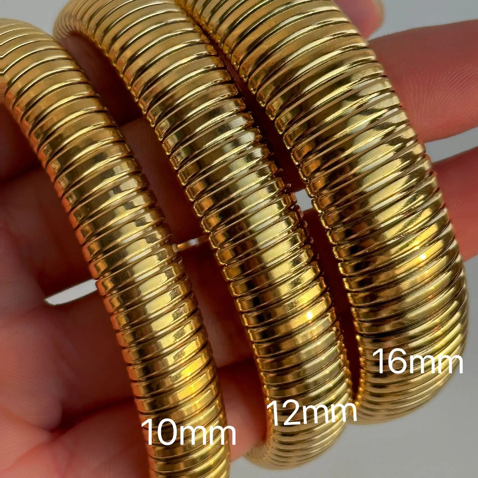 The image depicts a stylish bracelet with a ribbed design in a shiny rose gold color, suggesting it is made of 18k gold plated titanium. The bracelet features a twisted, interwoven appearance, giving it a unique and fashionable look. It appears to be a single, continuous band without clasps, showcasing its design.