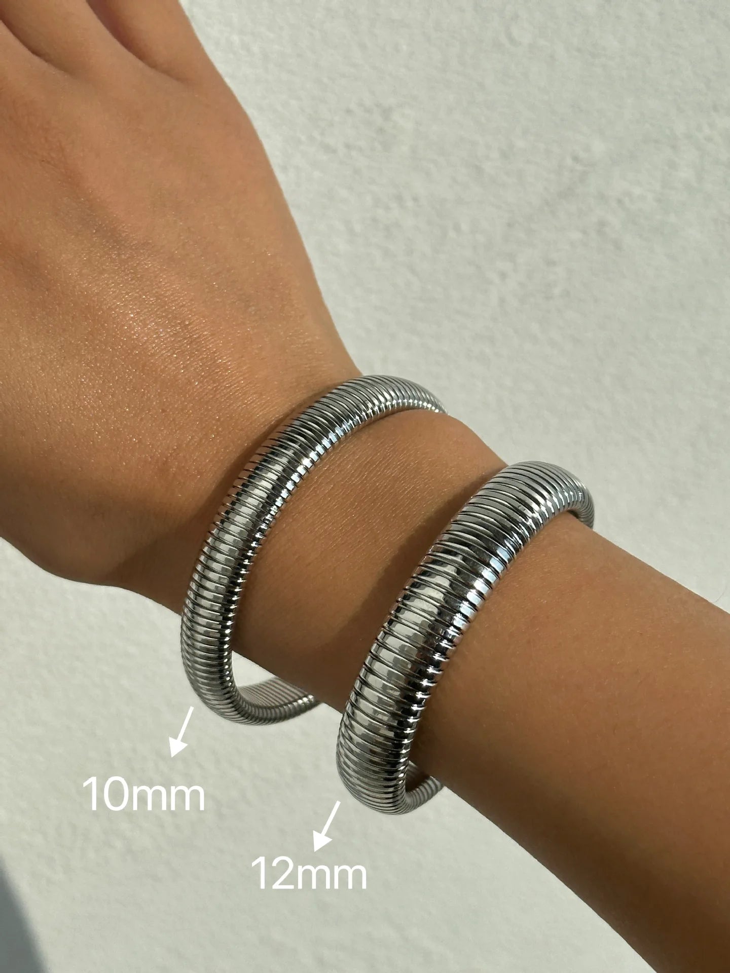 The image depicts a stylish bracelet with a ribbed design in a shiny rose gold color, suggesting it is made of 18k gold plated titanium. The bracelet features a twisted, interwoven appearance, giving it a unique and fashionable look. It appears to be a single, continuous band without clasps, showcasing its design.