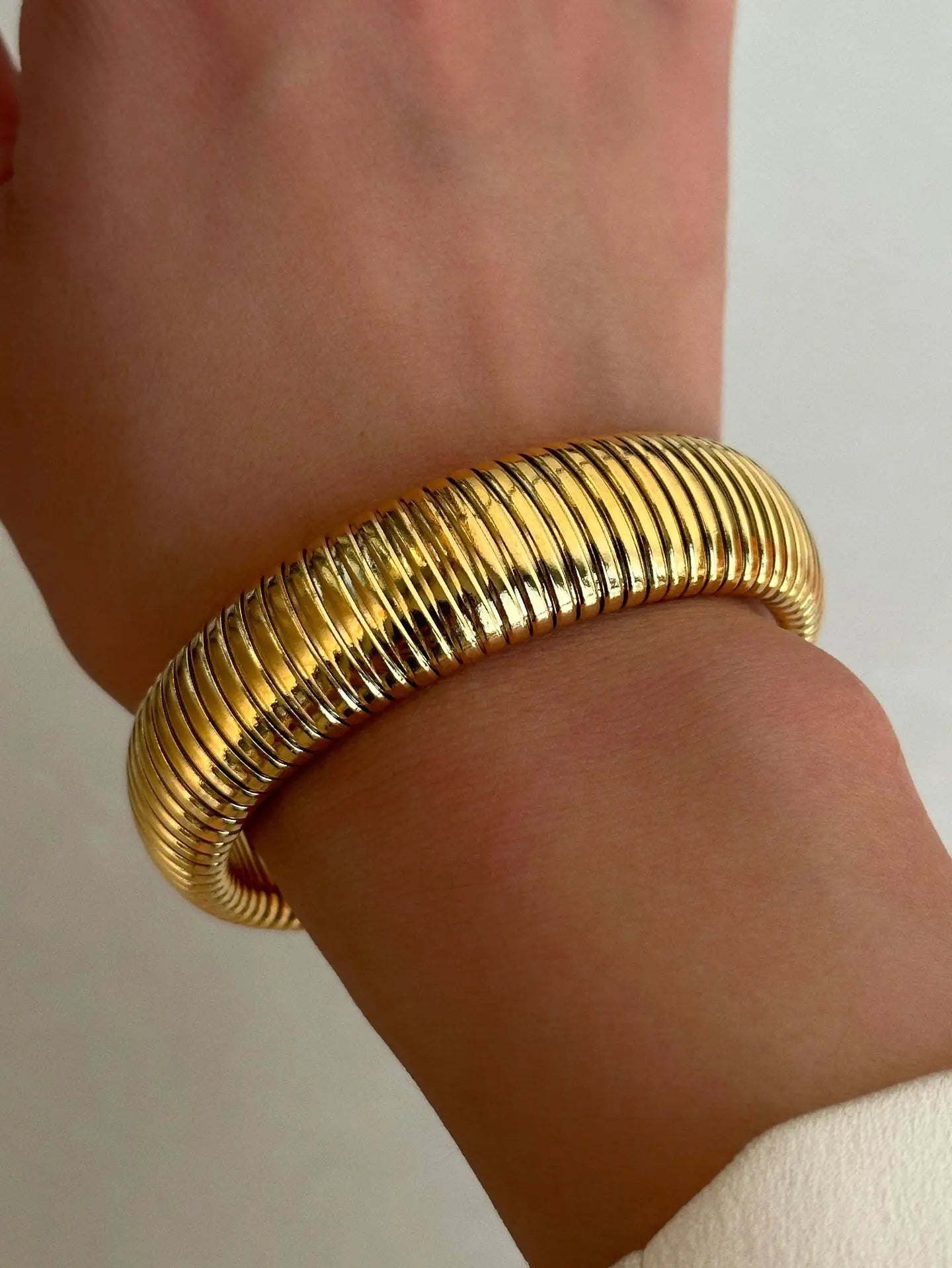 The image depicts a stylish bracelet with a ribbed design in a shiny rose gold color, suggesting it is made of 18k gold plated titanium. The bracelet features a twisted, interwoven appearance, giving it a unique and fashionable look. It appears to be a single, continuous band without clasps, showcasing its design.