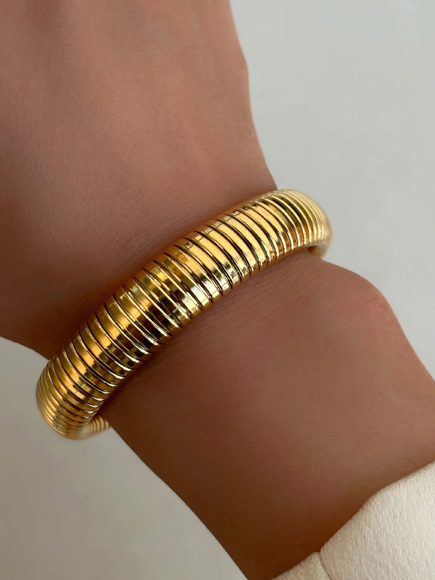The image depicts a stylish bracelet with a ribbed design in a shiny rose gold color, suggesting it is made of 18k gold plated titanium. The bracelet features a twisted, interwoven appearance, giving it a unique and fashionable look. It appears to be a single, continuous band without clasps, showcasing its design.