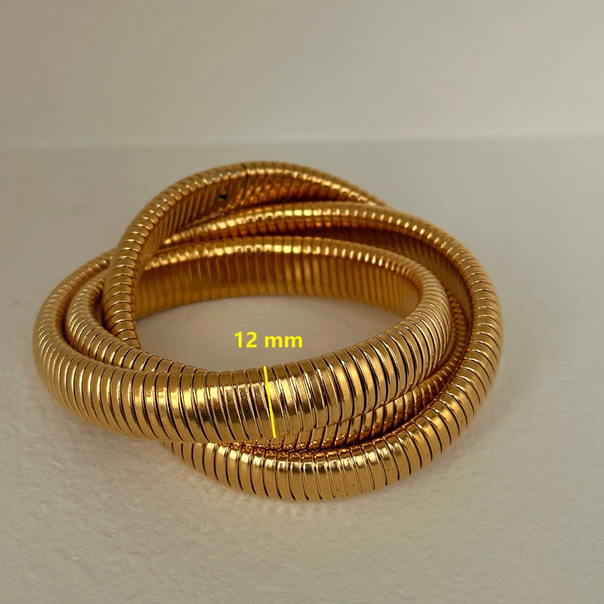 The image depicts a stylish bracelet with a ribbed design in a shiny rose gold color, suggesting it is made of 18k gold plated titanium. The bracelet features a twisted, interwoven appearance, giving it a unique and fashionable look. It appears to be a single, continuous band without clasps, showcasing its design.