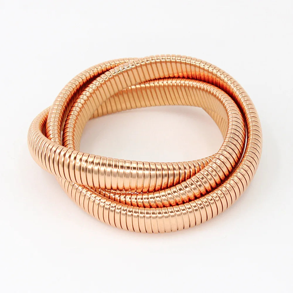 The image depicts a stylish bracelet with a ribbed design in a shiny rose gold color, suggesting it is made of 18k gold plated titanium. The bracelet features a twisted, interwoven appearance, giving it a unique and fashionable look. It appears to be a single, continuous band without clasps, showcasing its design.