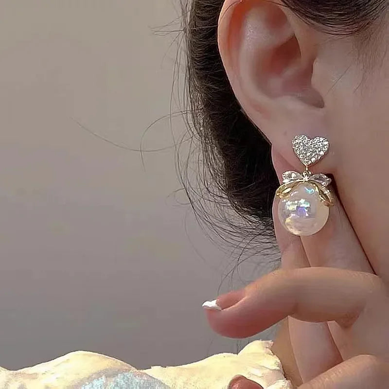 These earrings feature a delicate, sculpted design with a lovely floral motif. The main component is a graceful, curved shape that resembles the form of a flower petal. At the center, there is a smooth, spherical pearl bead that serves as the "bloom" of the floral design. The petal-like shape is made of a shiny, golden-toned metal that catches the light, creating an elegant, luminous effect.