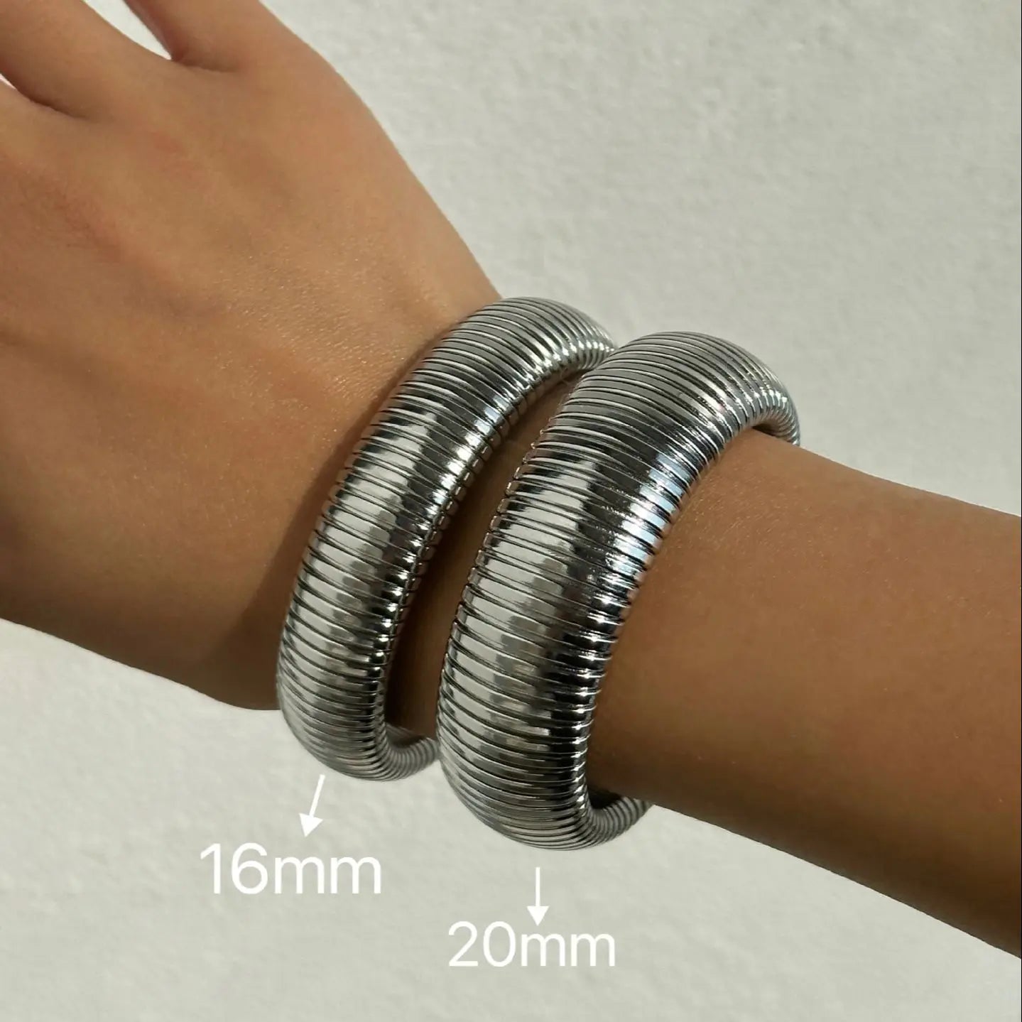 The image depicts a stylish bracelet with a ribbed design in a shiny rose gold color, suggesting it is made of 18k gold plated titanium. The bracelet features a twisted, interwoven appearance, giving it a unique and fashionable look. It appears to be a single, continuous band without clasps, showcasing its design.